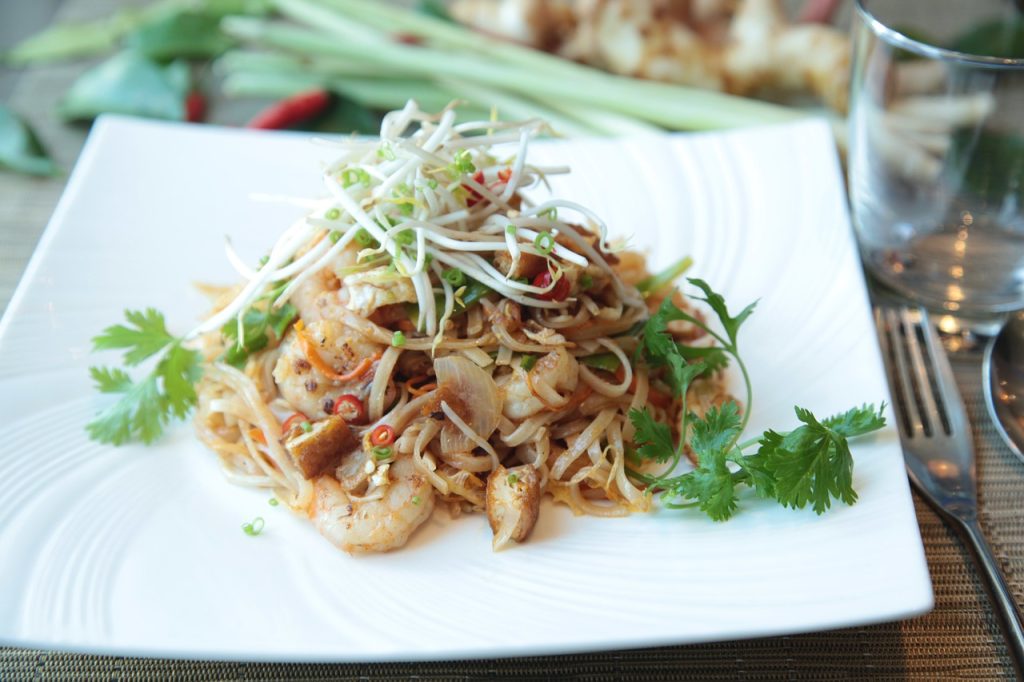 Plate of Quick Korean Pad Thai Noodles topped with colorful vegetables, sliced green onions, and sesame seeds, served in a vibrant bowl.