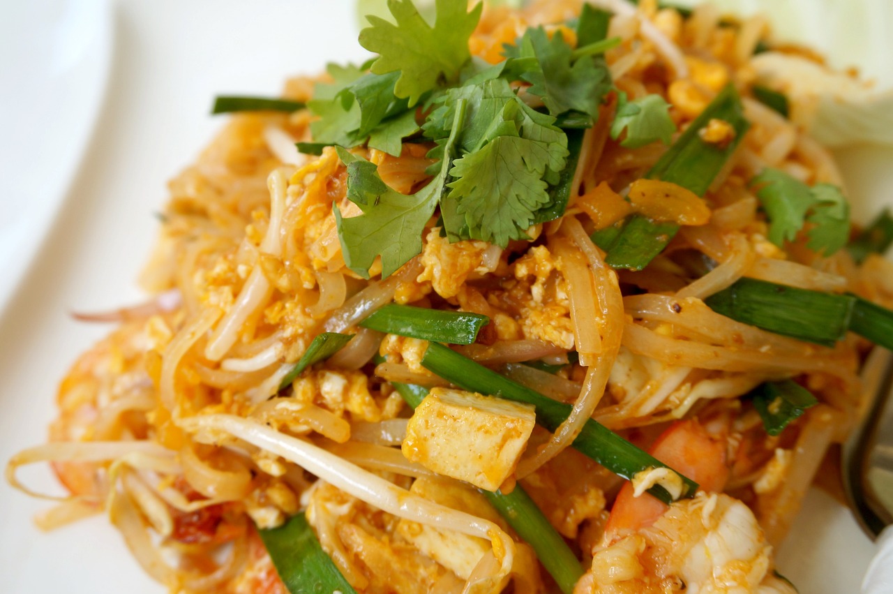 Plate of Quick Korean Pad Thai Noodles topped with colorful vegetables, sliced green onions, and sesame seeds, served in a vibrant bowl
