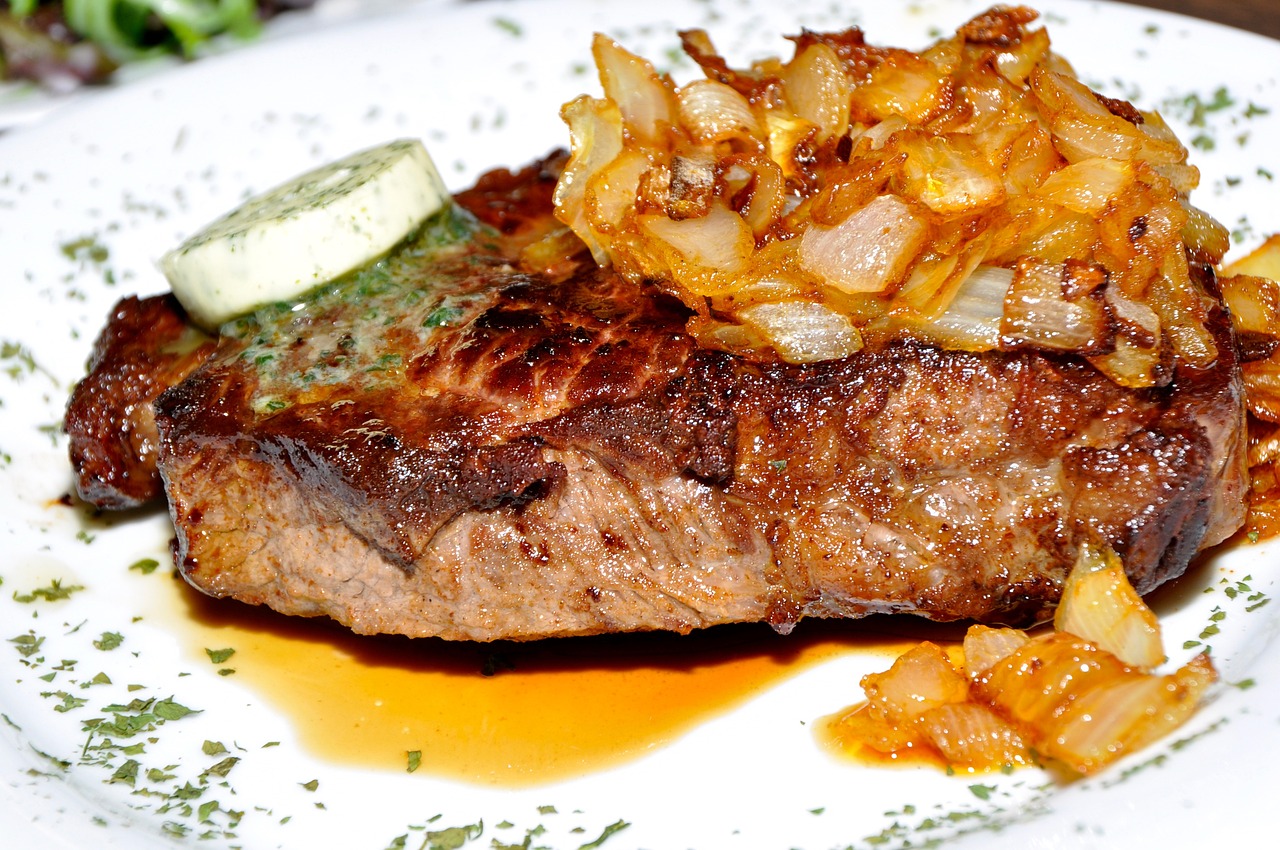 A perfectly seared steak with a golden-brown crust and juicy pink center, garnished with fresh herbs and a pat of melting butter.