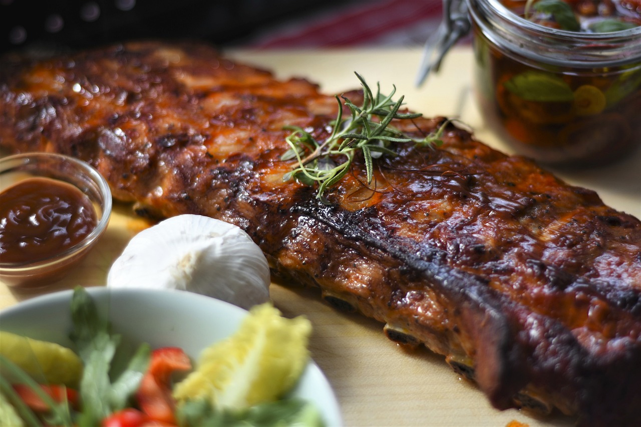 Juicy Smoked BBQ Ribs Platter – “A mouth-watering platter of juicy smoked BBQ ribs, garnished with fresh herbs and served with coleslaw and baked beans.” Essential BBQ Equipment – “A variety of BBQ tools arranged on a table, including a digital thermometer, spray bottle, foil, butcher paper, and BBQ rub ingredients.” Choosing Rib Cuts – “Close-up of baby back, spare, and St. Louis-style ribs laid out on a cutting board, highlighting the marbling and fat content of each cut.” Preparing Ribs with Dry Rub – “Raw ribs coated with a thick layer of brown sugar and spice rub, ready for the smoker.” Applying BBQ Rub – “Hands sprinkling a mix of spices over a rack of ribs on a cutting board, emphasizing the texture of the rub ingredients.” Low and Slow Smoking Process – “A smoker grill releasing a gentle plume of smoke with ribs cooking inside, set at a low temperature.” Spritzing Ribs – “A spray bottle misting apple juice over a rack of ribs, creating a shiny, caramelized surface.” Wrapping Ribs in Foil – “Ribs being wrapped tightly in foil on a table, showing the juices retained to keep the meat tender and moist.” BBQ Sauce Glazing – “Ribs on the grill with a brush applying a sticky, caramelized layer of BBQ sauce over the meat.” Sliced BBQ Ribs Ready to Serve – “Sliced BBQ ribs served on a wooden board with cornbread and grilled vegetables, ready to enjoy.”