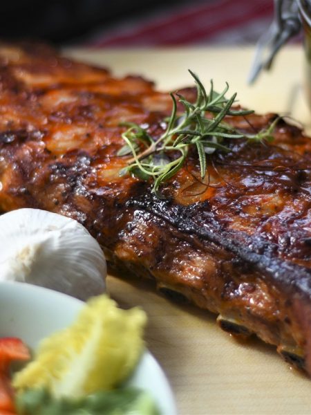 Close-up of perfectly smoked BBQ ribs with a caramelized glaze on a wooden cutting board" "Juicy, tender BBQ ribs with grill marks, topped with BBQ sauce and garnished with herbs" "Sliced BBQ ribs with a smoky, glazed crust on a serving platter, perfect for a summer cookout" "Perfectly cooked BBQ ribs with a rich, caramelized exterior and side of BBQ sauce for dipping" "Rack of BBQ ribs on the grill, showcasing a golden-brown glaze and a smoky finish"