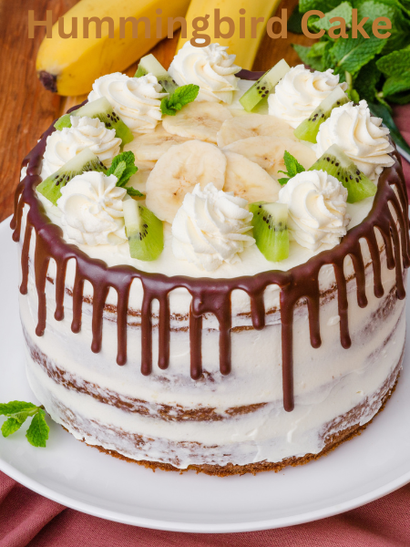 A moist and fluffy Hummingbird Cake topped with creamy frosting and chopped pecans on a white cake stand
