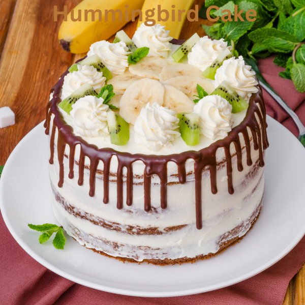 A moist and fluffy Hummingbird Cake topped with creamy frosting and chopped pecans on a white cake stand